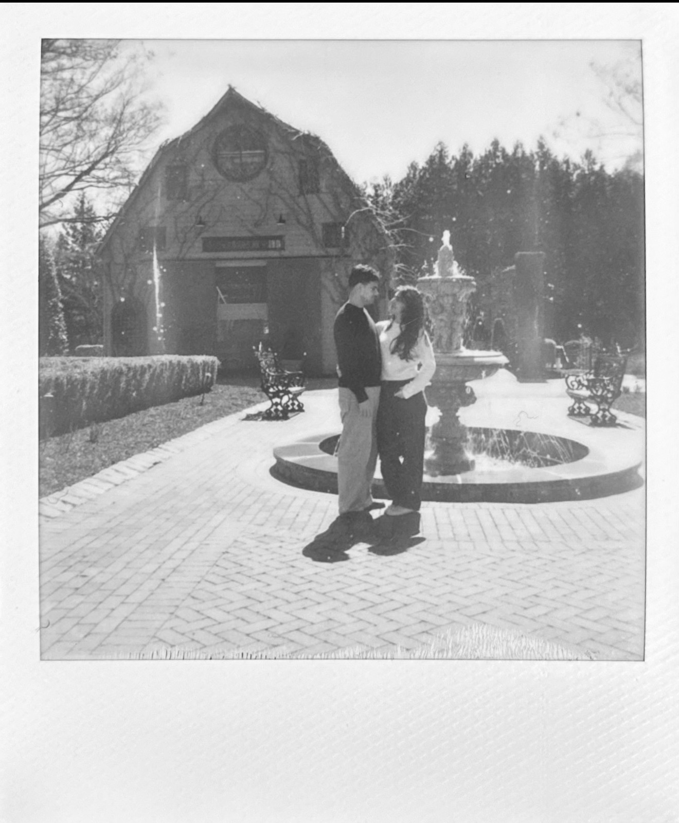 Katrina and Danny facing each other beside a fountain, in a black-and-white instant photograph